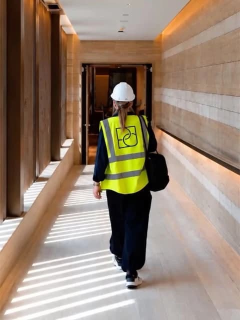 A designer wearing a Deboss Collective safety vest walks through a sunlit interior.